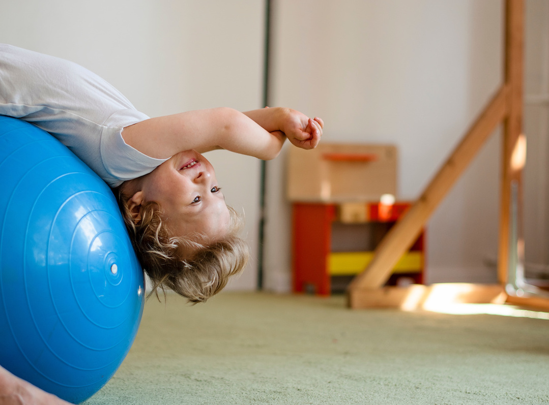 young toddler boy with curly hair lays back on an exercise ball